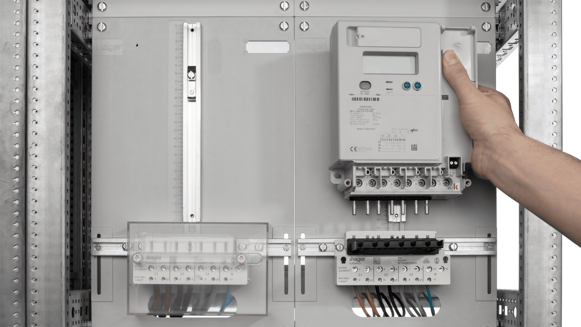 Die Hand einer Person installiert oder entfernt einen digitalen Stromzähler in einer Schalttafel mit mehreren Unterbrechern und freiliegenden Kabeln, die darunter sichtbar sind.