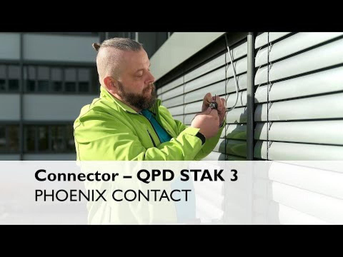 Un homme en veste verte installe des câbles sur un mur extérieur avec des lamelles métalliques horizontales. Le texte superposé est le suivant : Raccordement - QPD STAK 3 PHOENIX CONTACT.